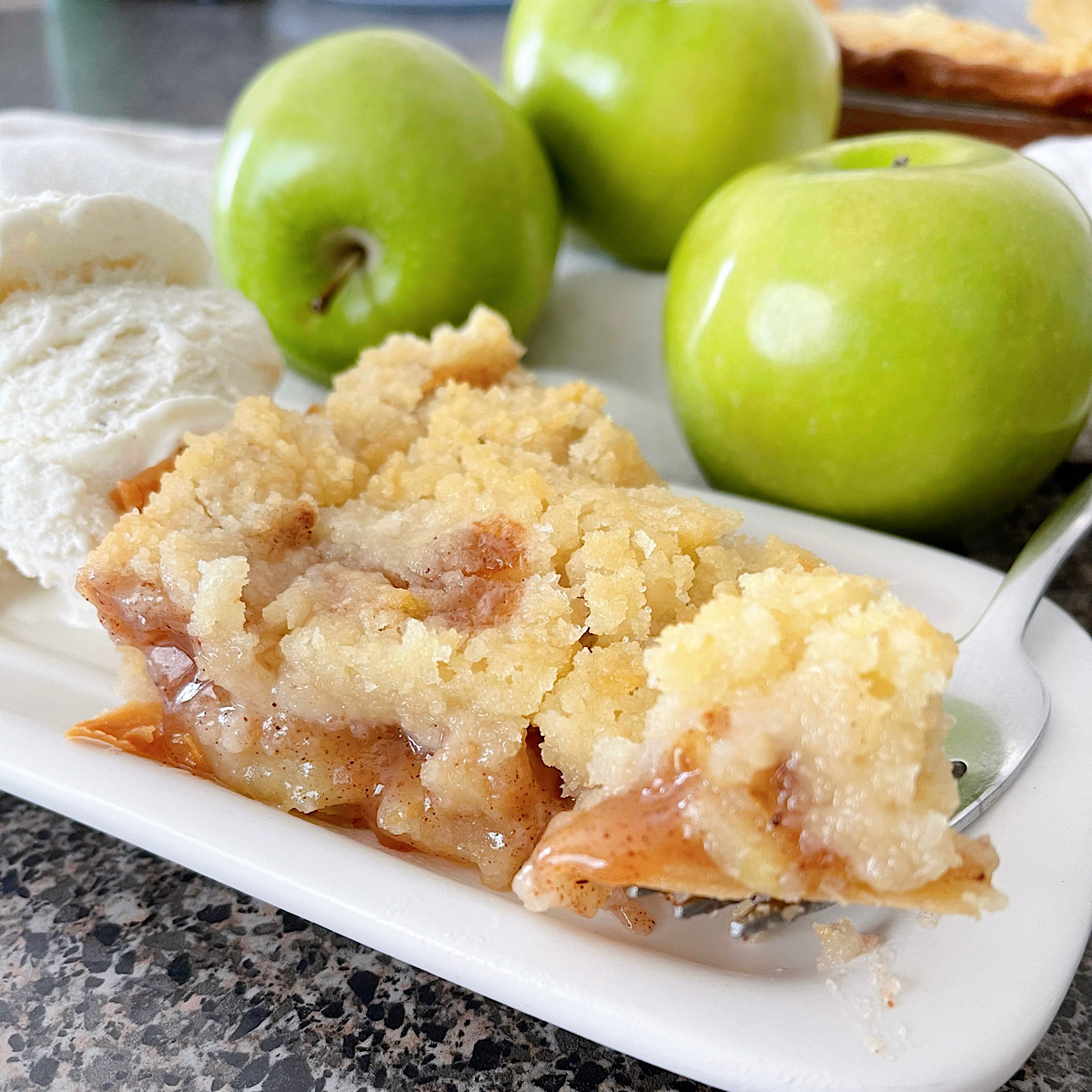 A slice of Dutch apple pie with three green apples and a scoop of ice cream.