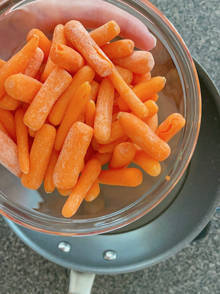 Raw baby carrots over a pan of water.