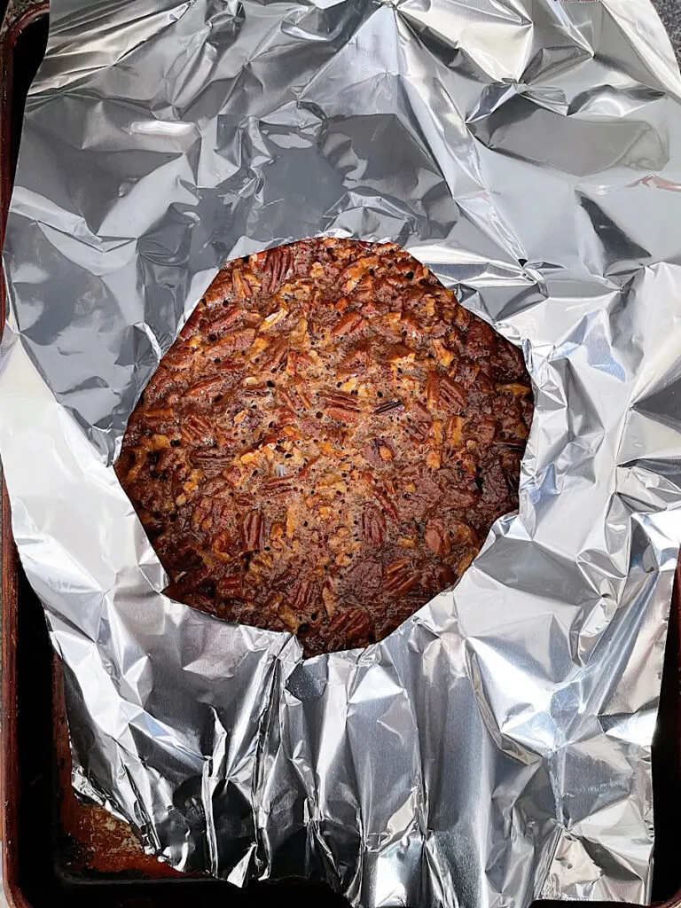 A pecan pie covered in foil, baking in an oven.