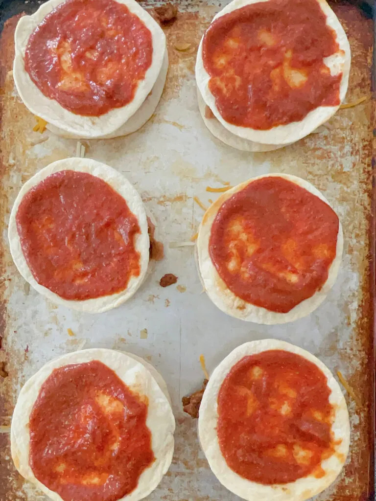 Tortillas with red sauce on a baking sheet.
