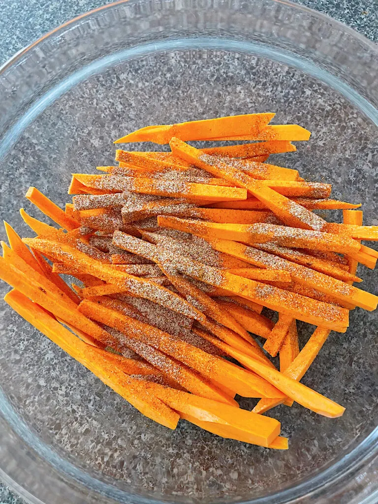 Sweet potato fries in a glass bowl with spices.