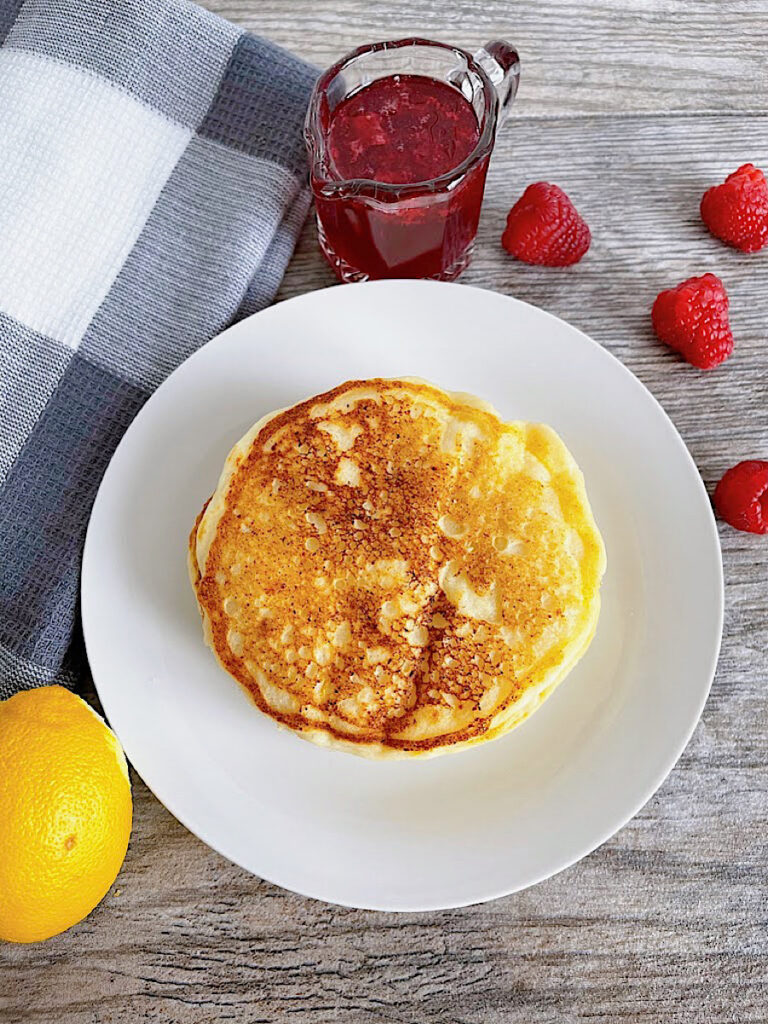 Lemon Ricotta Pancakes on a plate with raspberries and raspberry syrup.