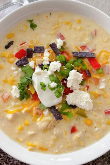 A bowl of Mexican Corn Chowder with sour cream, cilantro, green onion, and tortilla strips.