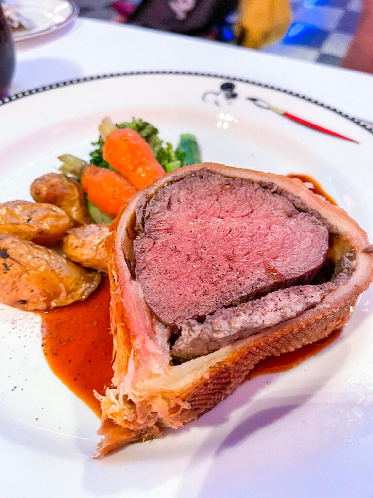 Roasted Filet of Beef Wellington: is covered with mushroom stuffing wrapped in puff pastry and is served with fingerling potatoes, baby vegetables, and a cabernet black truffle jus from Animator's Palate on the Disney Magic.