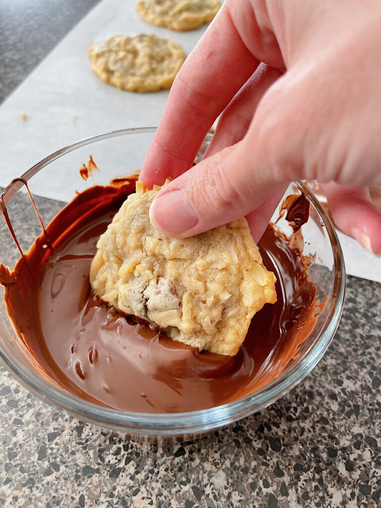 An almond joy cookie dipped in a bowl of melted chocolate.