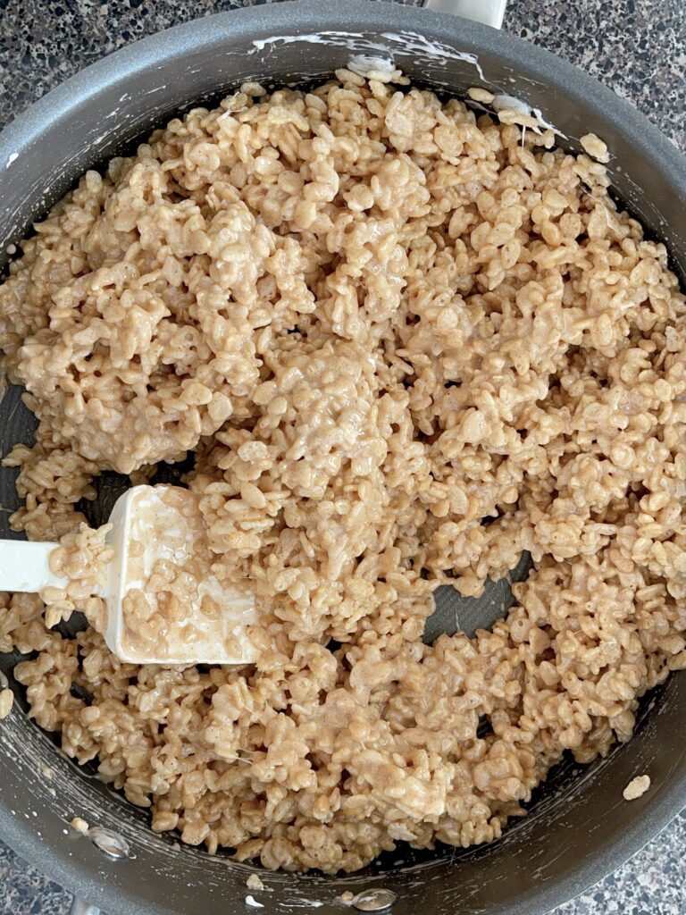 Rice Krispies mixed with melted marshmallow mix in a saucepan.