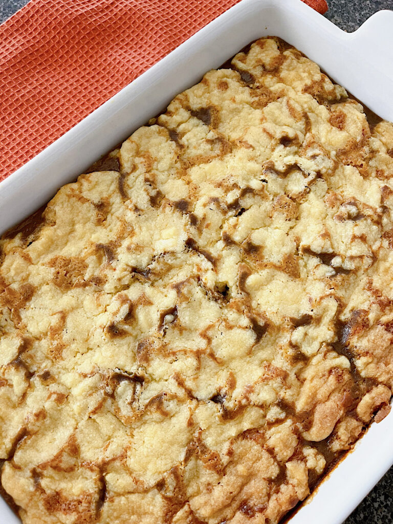 A baked cake mix pumpkin cobbler in a white dish with a dark orange towel.