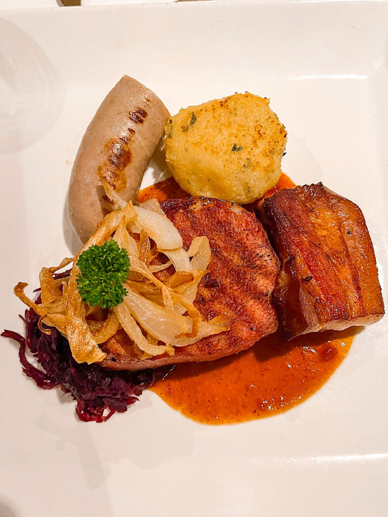 Flynn Rider Platter: Grilled Smoked Pork Belly, Brockwurst, Braised Red cabbage, and fried potato dumpling from Rapunzel's Royal Table on the Disney Magic.