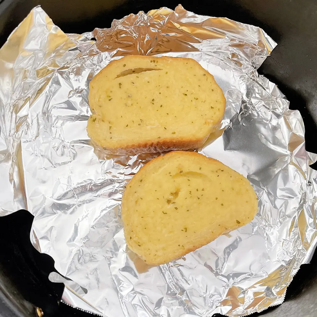 Two slices of garlic bread on foil in an air fryer.