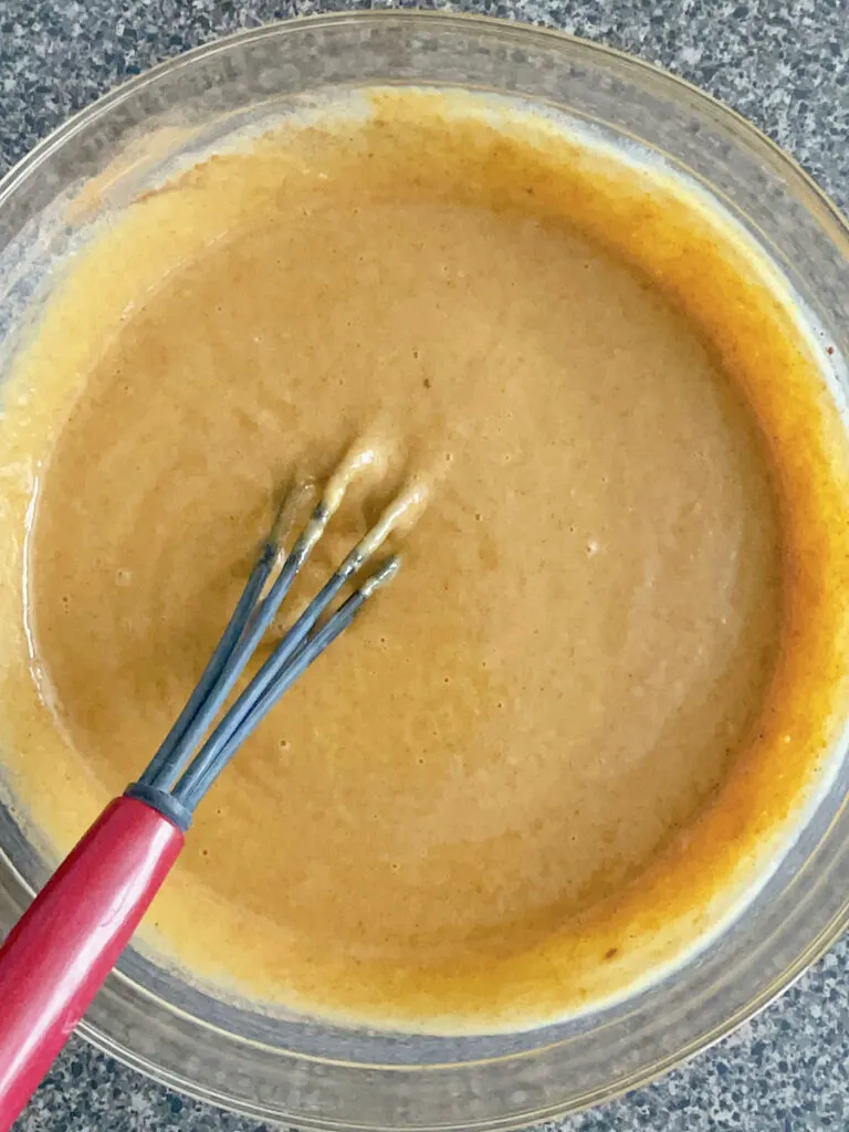 Pumpkin cobbler batter with a whisk in a glass bowl.