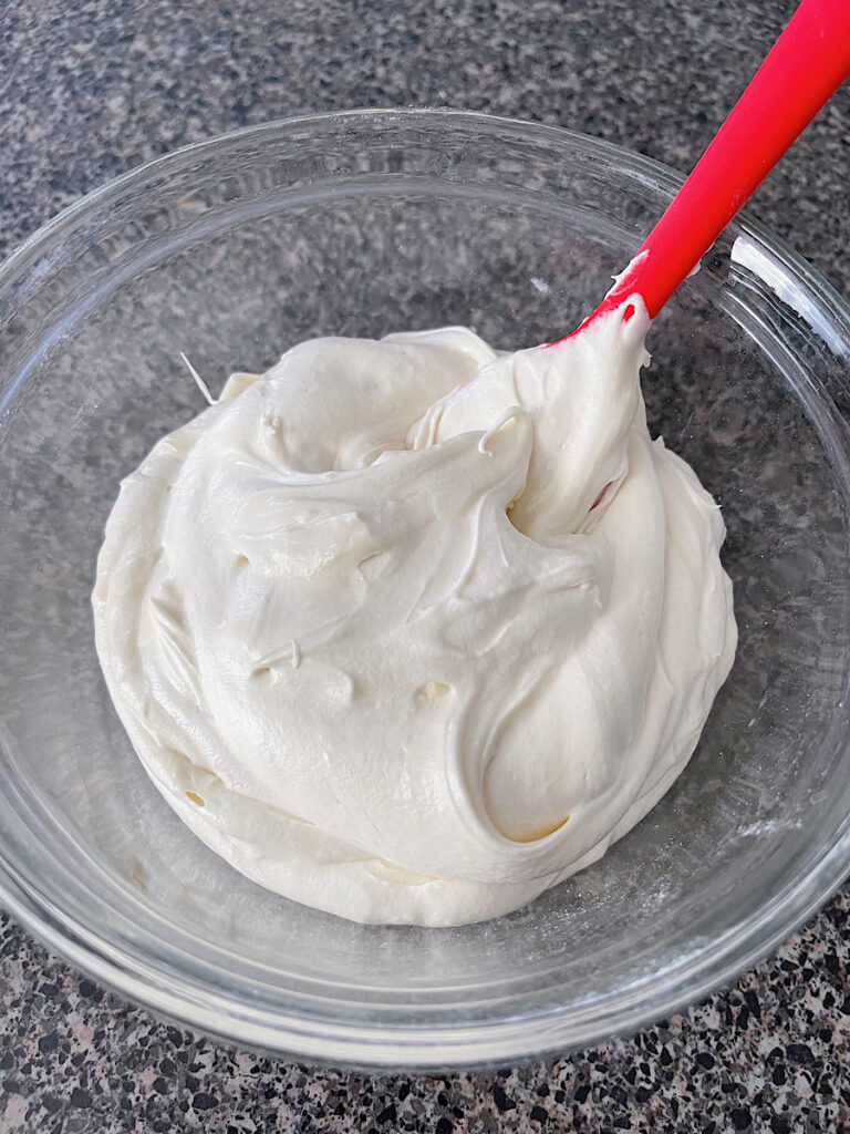 A bowl of cream cheese frosting with a red spatula.