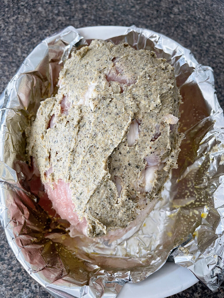 Butter and herbs spread on a turkey in a roasting pan.