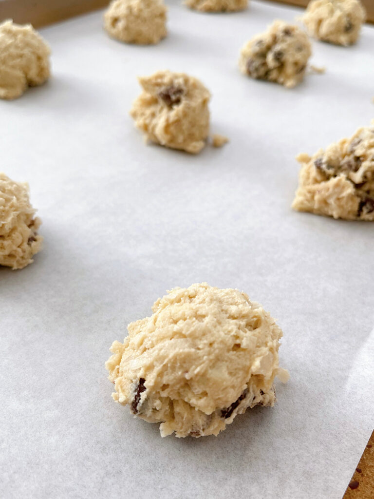 Balls of almond joy cookie dough on a parchment paper lined baking sheet.