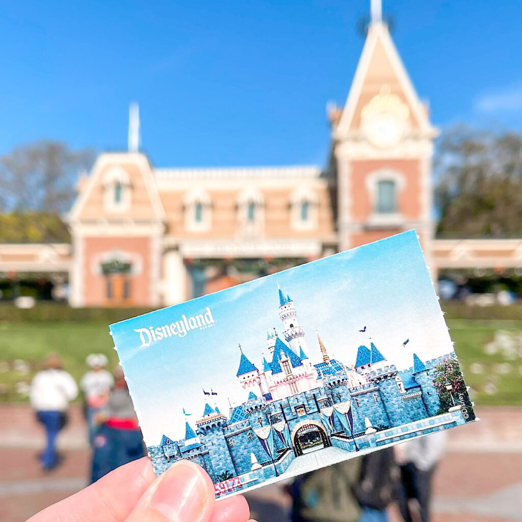 Someone holding a Disneyland Ticket in front of the Disneyland Train Station.