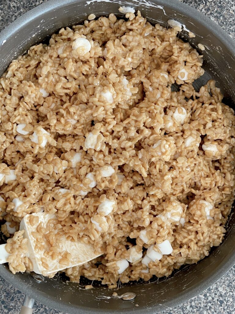 Rice Krispies mixed with melted marshmallow mix in a saucepan.