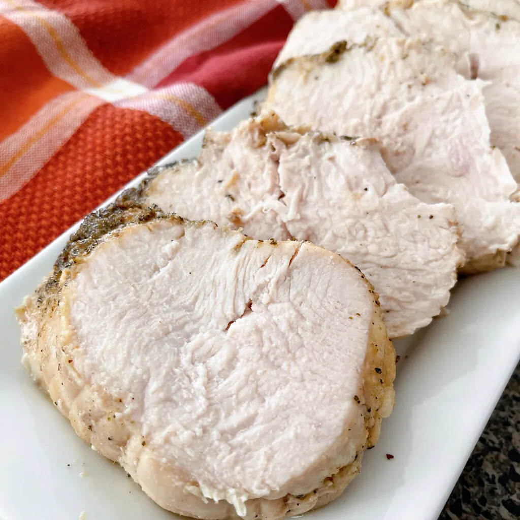 Slices of butter & herb roasted turkey on a white plate.