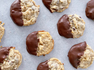 Almond joy cookies dipped in chocolate on parchment paper.