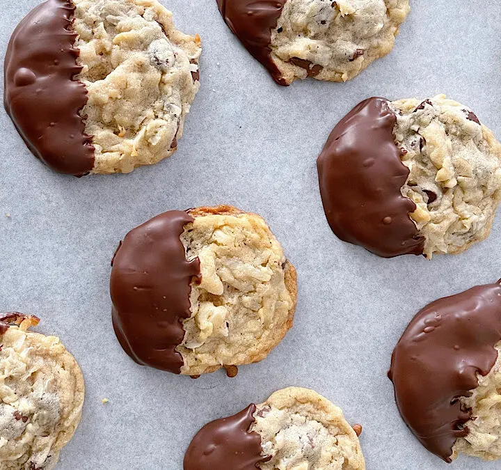Almond joy cookies dipped in chocolate on parchment paper.