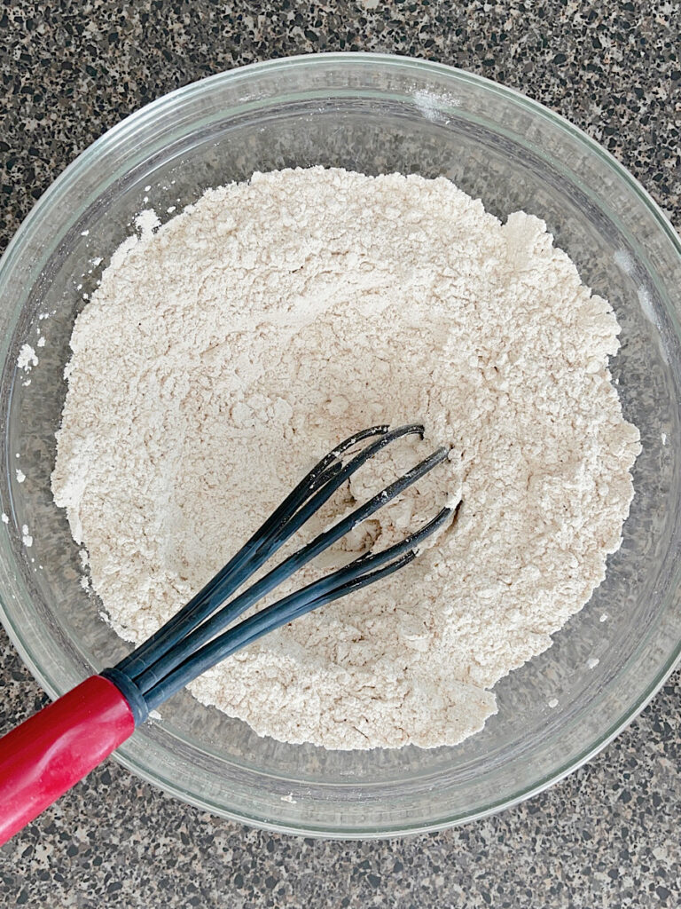 Dry ingredients for pumpkin bars in a glass bowl with a whisk.