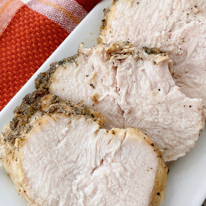 Slices of butter & herb roasted turkey on a white plate.