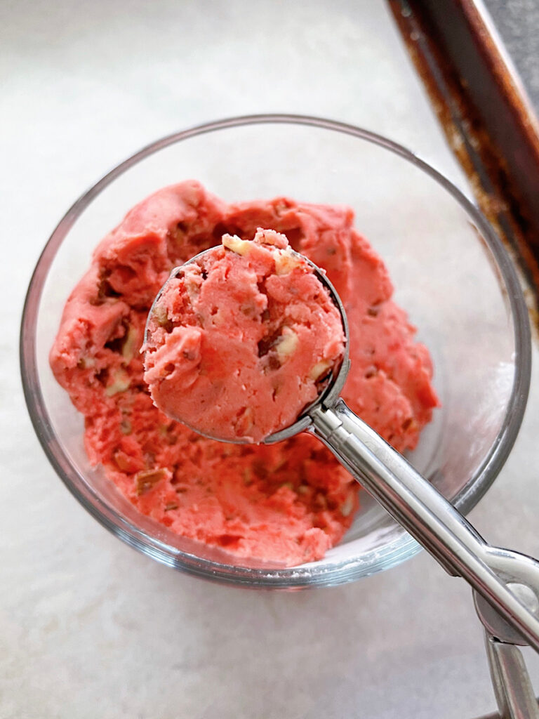 Red snowball cookie dough in a cookie scoop.
