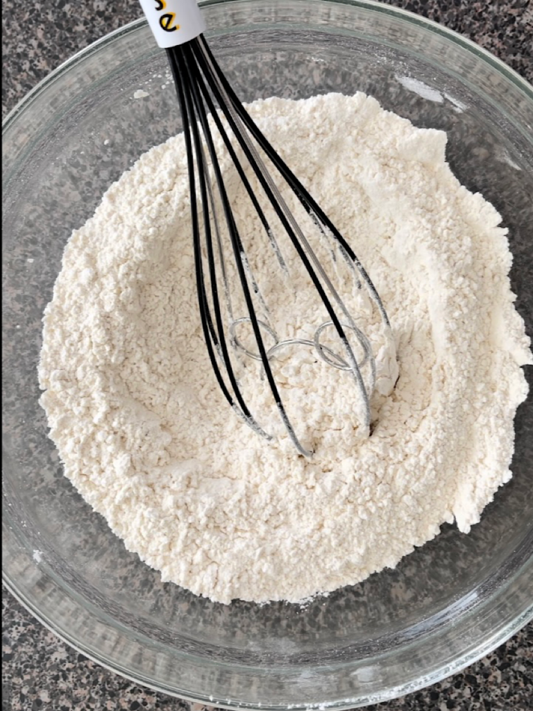 Flour and baking powder in a bowl with a whisk.
