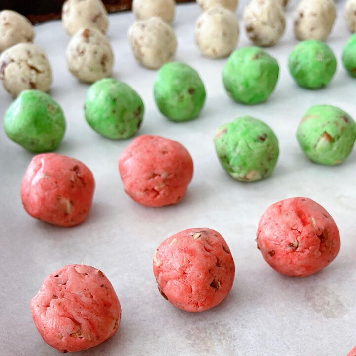 Red, green and white Christmas Snowball Cookies on a parchment paper lined baking sheet.