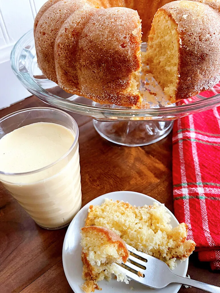 A slice of eggnog bundt cake with a glass of eggnog.