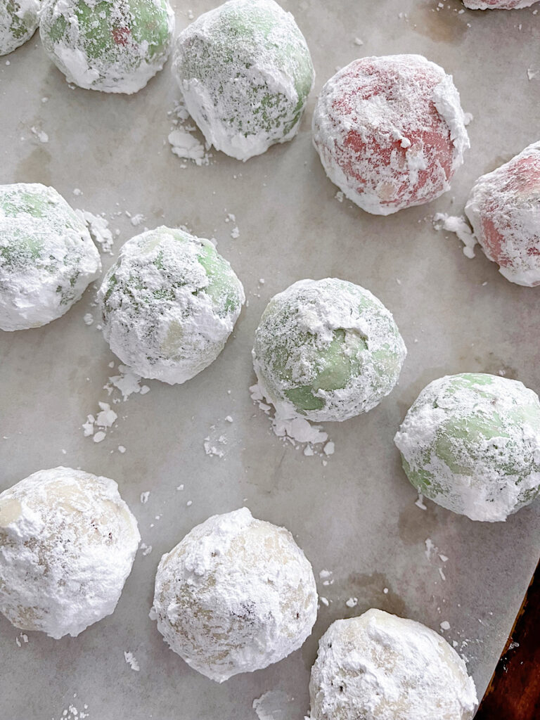 Red, green and white Christmas Snowball Cookies covered with powdered sugar on a parchment paper lined baking sheet.