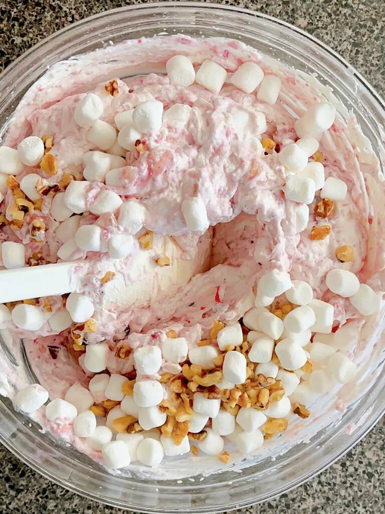 A bowl of cranberry fluff salad with marshmallows and walnuts.