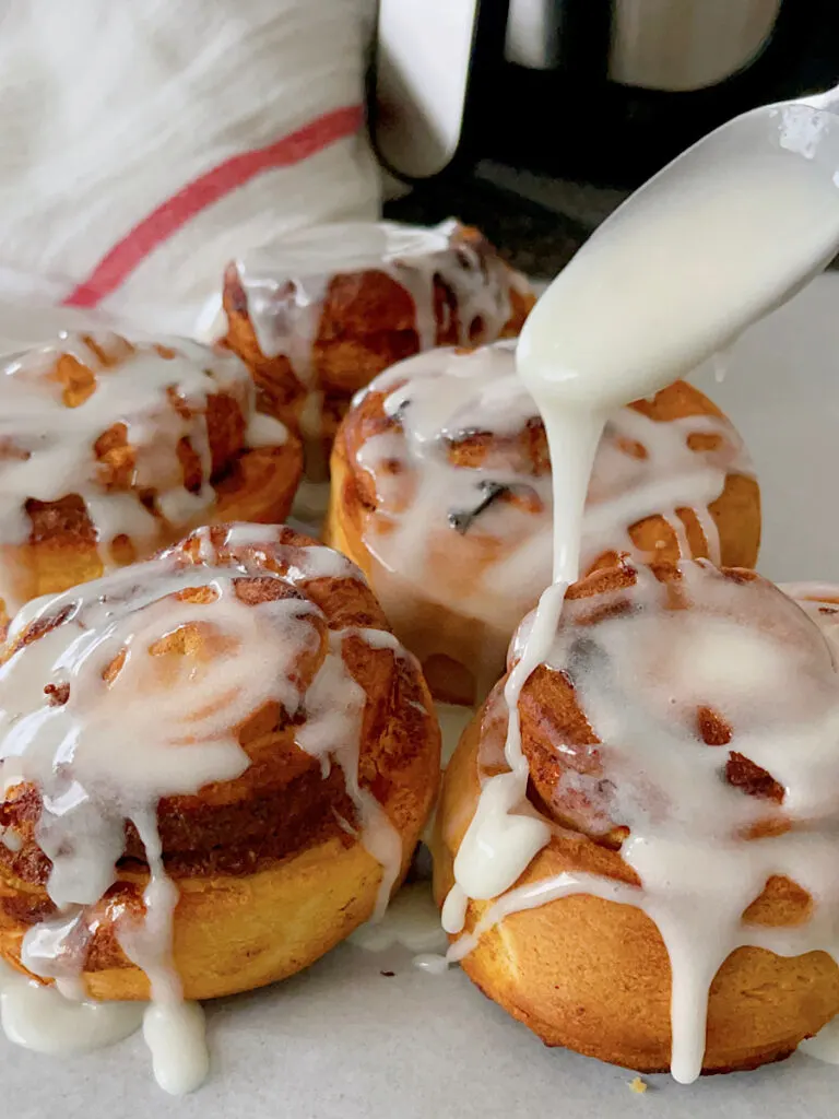 Frosting being drizzled over cinnamon rolls baked in an air fryer.