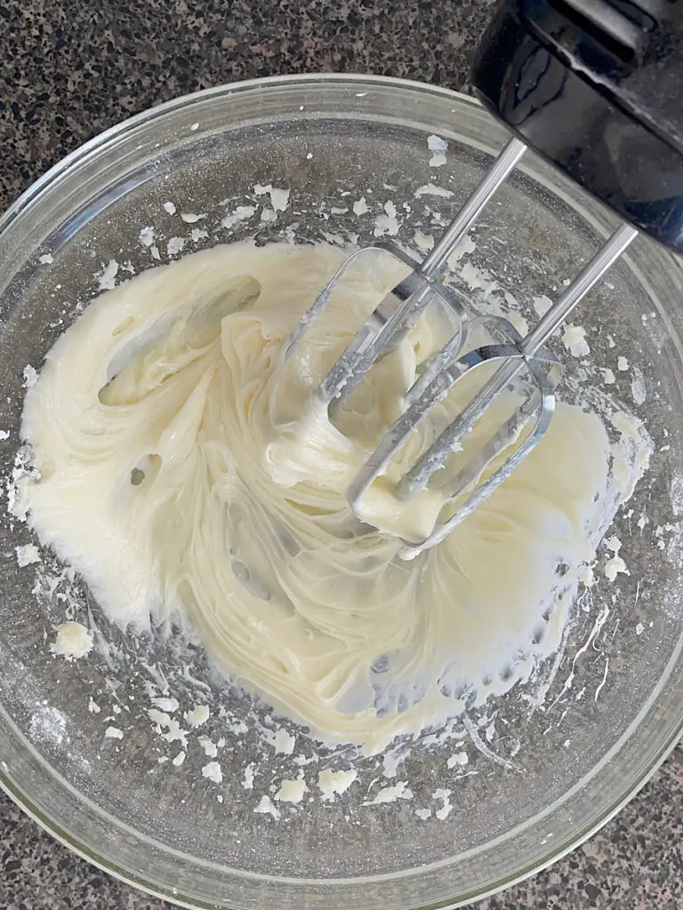 Cream cheese in a mixing bowl with a hand mixer.
