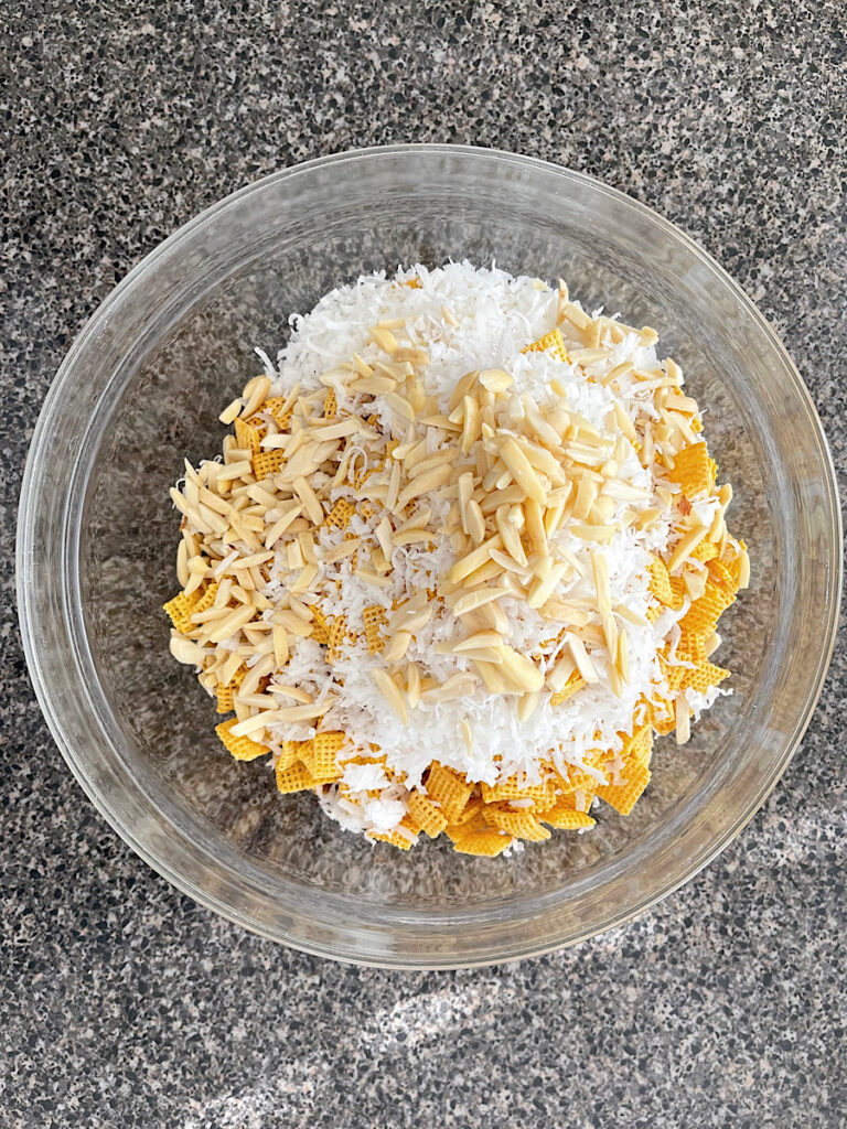Golden Grahams, Chex, coconut, and almonds in a glass bowl.
