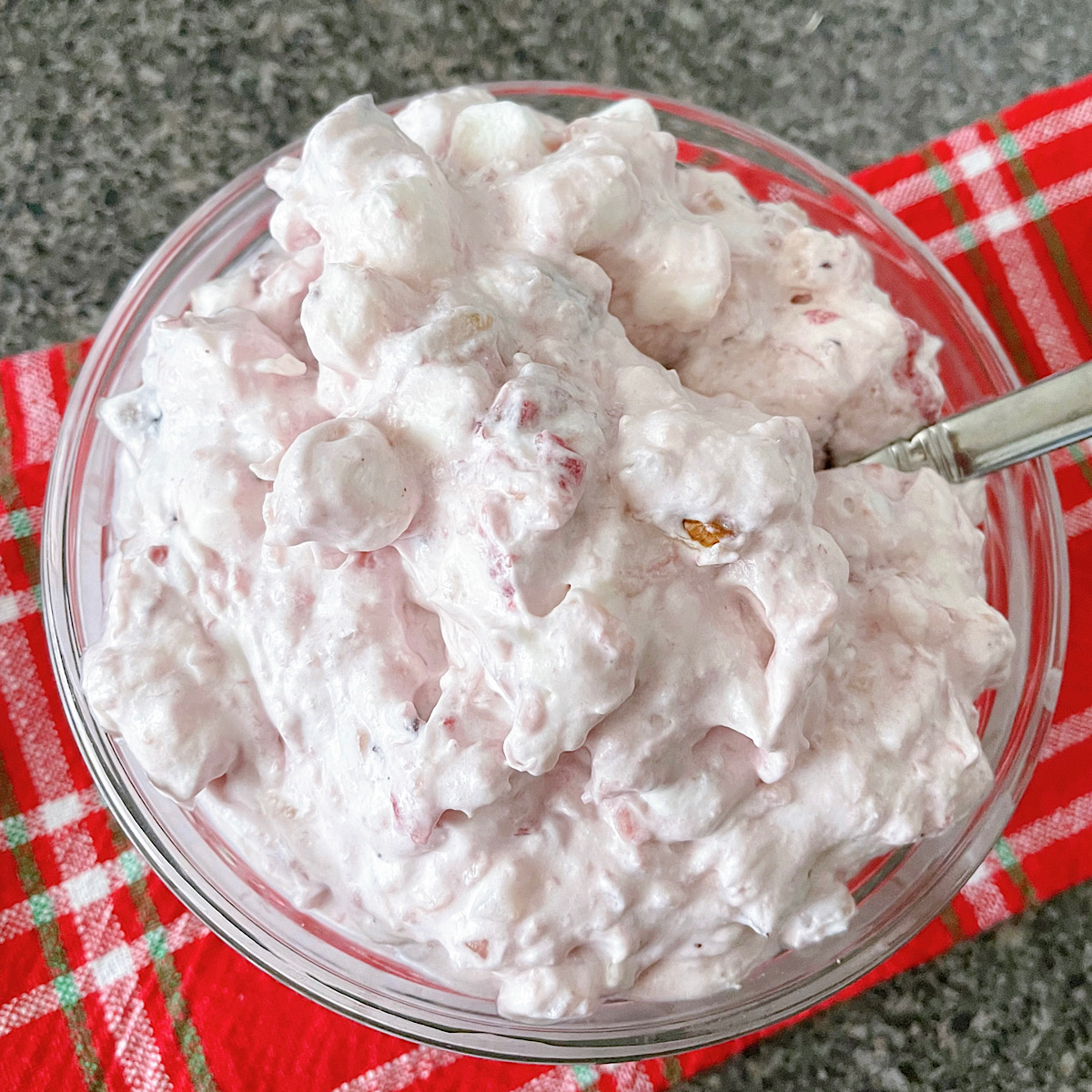 A bowl of Thanksgiving cranberry salad with a spoon on a red and white towel.