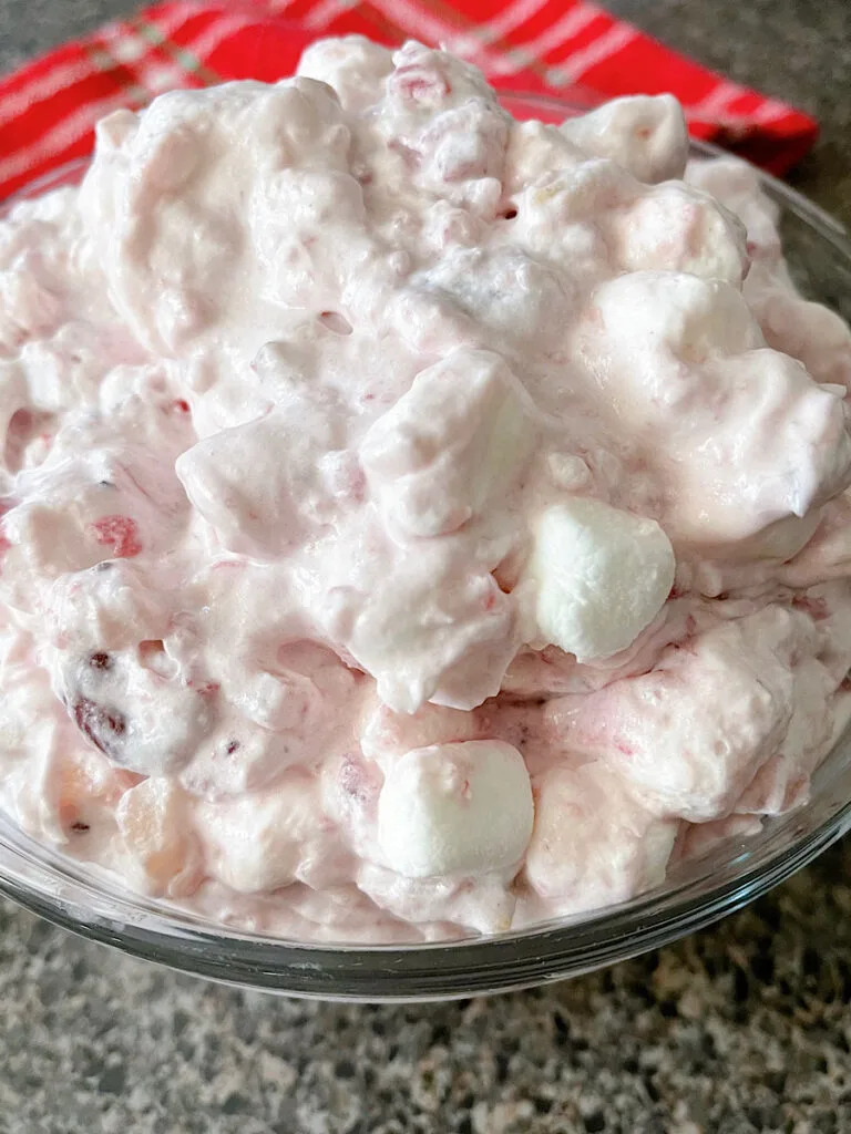 A bowl of cranberry fluff salad with marshmallows and walnuts.