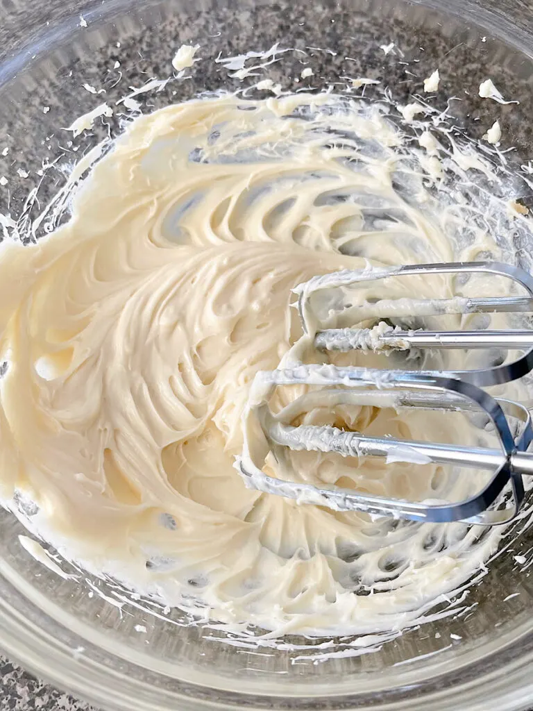 Cream cheese mixed with sugar in a bowl with a hand mixer.