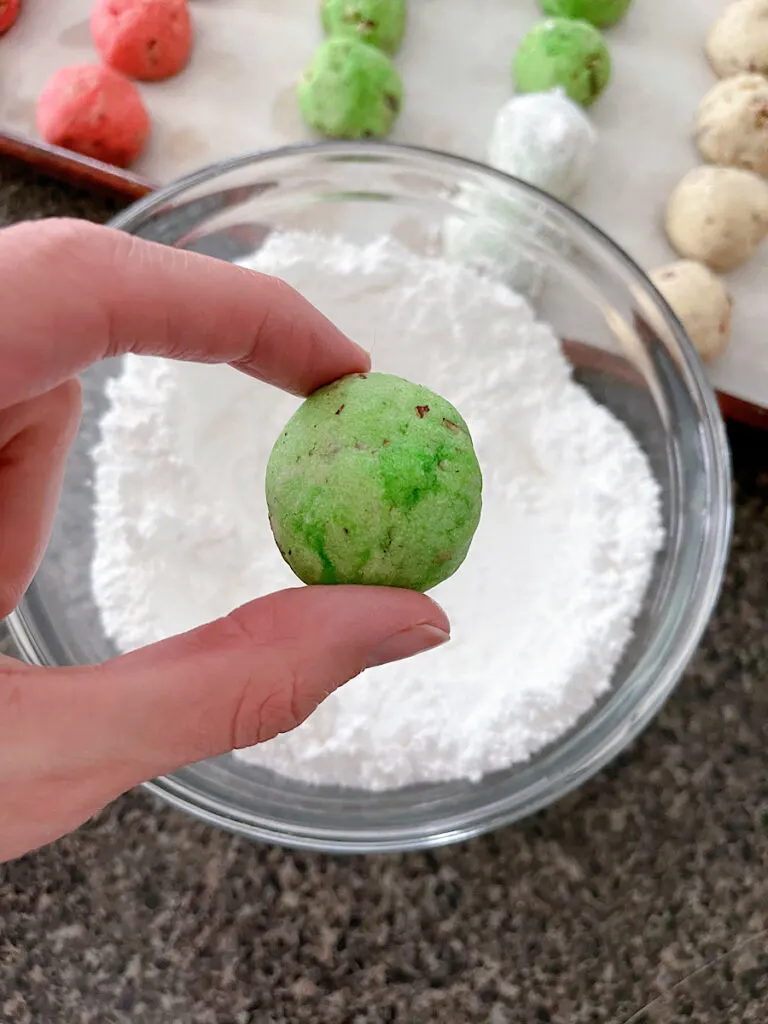 A green snowball cookie over a bowl of powdered sugar.