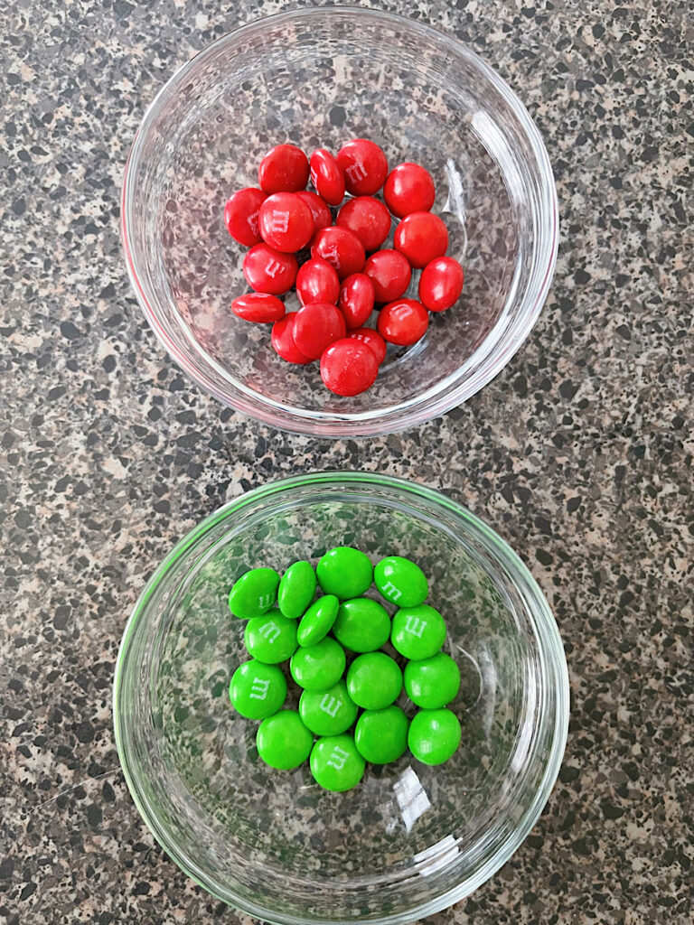 A bowl of red M&Ms and a bowl of green M&Ms.