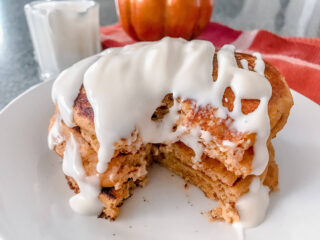 A stack of pumpkin pancakes drizzled with cream cheese syrup.