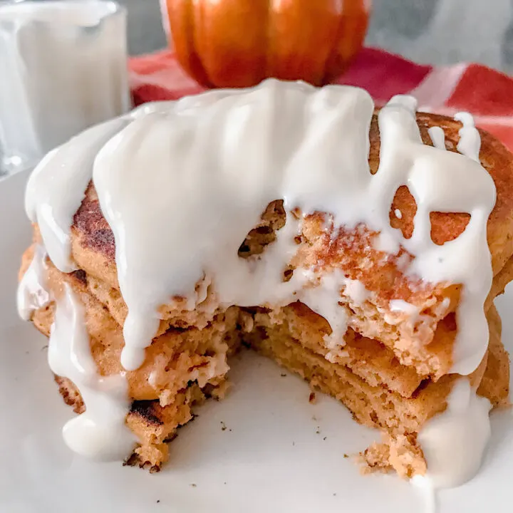A stack of pumpkin pancakes drizzled with cream cheese syrup.