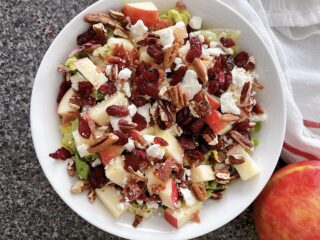 A salad in a bowl with lettuce, apples, bacon, feta cheese, and dried cranberries.