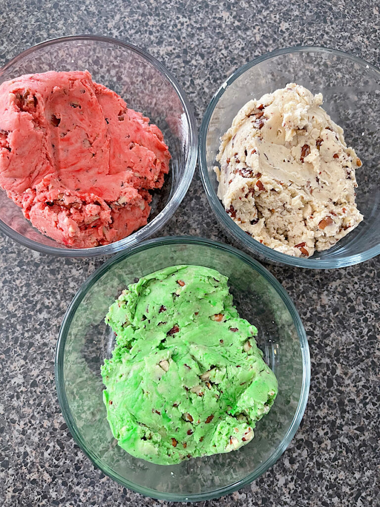 A bowl filled with green snowball cookie dough, red dough, and plain snowball cookie dough.