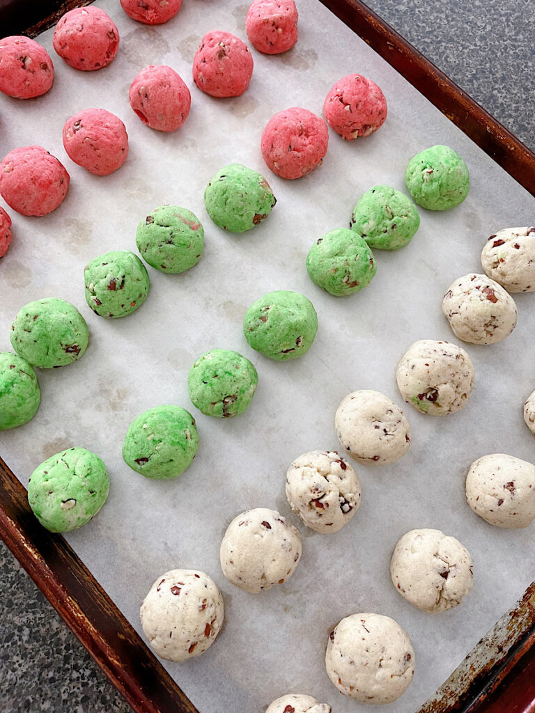 Red, green and white Christmas Snowball Cookies on a parchment paper lined baking sheet.