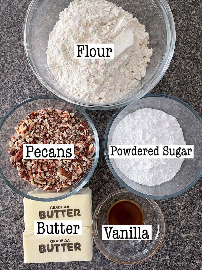 Ingredients in bowls including flour, pecans, powdered sugar, butter, and vanilla for Christmas Snowball Cookies.