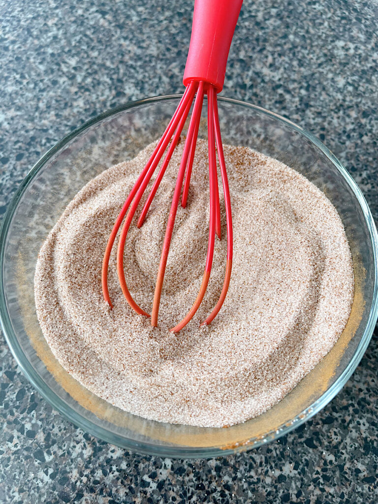 A bowl of cinnamon sugar with a red whisk.