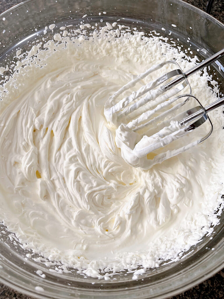 A bowl of whipped cream with a hand mixer.