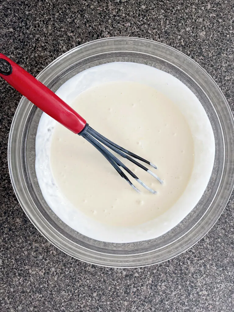 Wet ingredients to make sweet cream pancakes in a mixing bowl with a whisk.