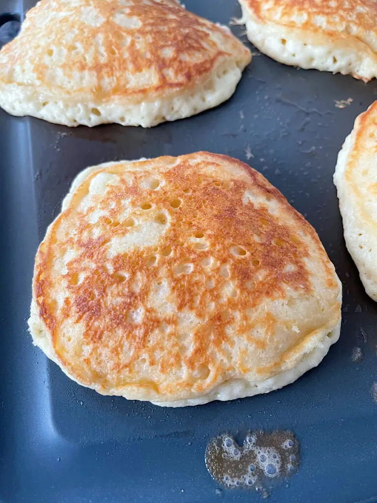 Sweet cream pancakes cooking on a griddle.