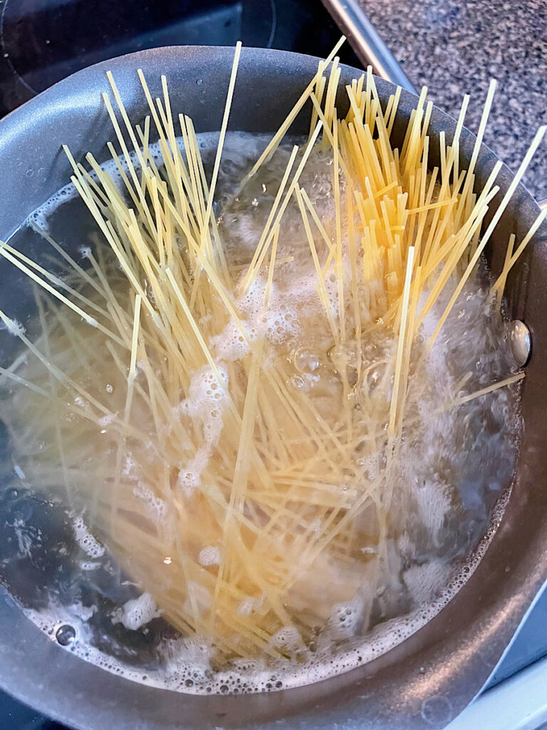 Spaghetti noodles cooking in a pan of water.
