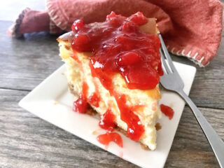 A slice of New York style cheesecake topped with strawberry sauce.